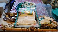 Wide view of multiple plastic bins and containers filled with folded fabric pieces and patterns on a bedspread.