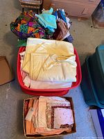 Photo of a red plastic bin filled with colorful and light fabric pieces, including a multicolored patchwork fabric on top