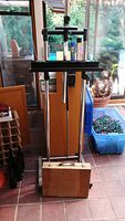 Front view of metal artist easel with wooden paint box placed at its base and oil paint tubes on the easel shelf.