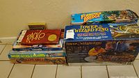 Photo showing stack of seven boxed games including Forbidden Bridge, Tower of the Wizard King, Racko, Dweebs, and Geeks & Weirdos.