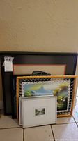 Grouped view of three framed artworks against beige wall showing relative sizes and frame materials.