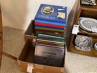 Vinyl record sets including a blue Dvorak classical collection box and colorful History of Music in Sound boxed albums stacked in cardboard boxes on carpeted floor.