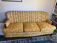 Front view of the vintage floral sofa showing the three seat cushions, floral upholstery, tufted backrest, and wooden legs.