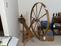 Wooden spinning wheel with 38-inch diameter wheel and treadle, positioned beside books and boxes.