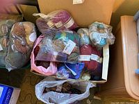 Box containing a variety of multicolored wool yarn skeins mostly in plastic packaging.