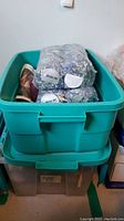 Two plastic bins stacked with the top bin containing yarn including large unopened plastic bags of Mister Joe yarn visible on top.