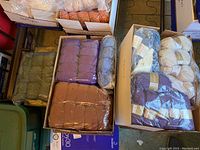 Overhead view of boxes containing yarn skeins in purple, blue, brown, olive green, and peach shades mostly in plastic wrap.
