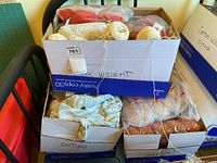 Top-down view of three boxes filled with yarn and partially completed knitting projects showing mixed yarn types and colors.