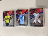 Three soccer trading cards in protective sleeves, displaying players Giovani Reyna, Kevin De Bruyne, and Armindo Sieb from the Topps Finest series.
