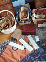 Photo showing baskets of various sizes, two Asian keepsake boxes, carved wood trays, and three embroidered satin placemats on a patterned rug.