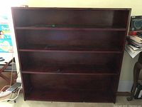 Front view of solid wood four shelf bookcase showing three upper shelves and base compartment. Dark stained wood with visible wear.