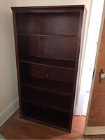 Full front view of the dark stained wooden bookcase showing four shelves and crown molding top.