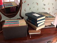 Books arranged on wood dresser with floral wallpaper background, showing boxed set of religion books and stacked hardcovers.