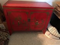 Front view of red painted wooden chest with hand-painted Asian-themed designs on cabinet doors, shows condition including surface scratches and chips.