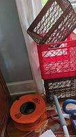 Stacked milk crates and orange outdoor extension cord coiled on floor next to wall and curtain.