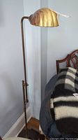 Full view of the copper tone floor lamp with clam shell shaped shade and adjustable height feature, showing the lamp in position next to furniture.