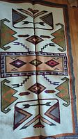 Full view of handmade ethnic wool kilim showing geometric ethnic patterns with arrows and angular designs in vibrant colors on a cream background.