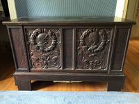 Front view of antique oak marriage chest showing carved panels of man and woman profiles.