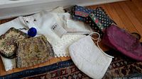 Full view of all items on wood floor with white embroidered tablecloth in center, showing purses, wallets, glass ornament and pillowcase.