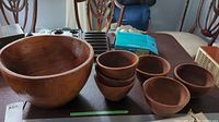 Photo of the large teak bowl and six smaller bowls on a table, showing the condition and natural wood grain.