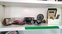 Shelf with all items: Seiko watch in box, Seth Thomas travel alarm clock, model cars and carved stone mill wheel