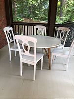 Round white Formica top table with natural wood legs surrounded by five painted wooden chairs showing paint chipping.