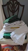 Stack of various folded linens on a chair, including white guest towels with lace and monogramming, green and yellow cloths.