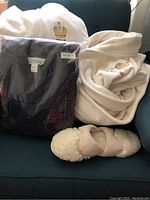 Two white embroidered bath robes on blue chair, one sealed in plastic, with beige slippers below.