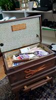 Opened vintage wooden sewing chest showing interior contents including scissors, patterns, and notions.