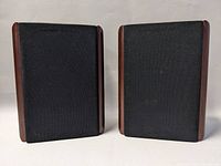 Front view of the pair of Centrios bookshelf speakers showing the black fabric grills and wood side panels.