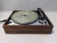 Side-angle photo showing the wooden casing, metal platter, tonearm, and control panel of the Dual 1219 turntable.