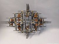 Full view of the metal wall sculpture showing its symmetrical, layered geometric form and color details.