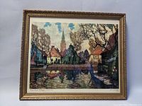 Framed aquatint etching artwork depicting a village scene with water reflection, signed and titled on the margins.