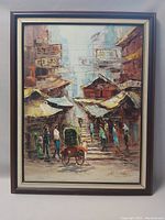 Framed oil on board painting showing a detailed Hong Kong street scene with people and market stalls. Signature of artist Charles Chan visible in lower right corner.