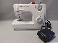 Side view of white Singer Prelude sewing machine with two control dials and foot pedal visible