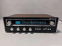 Front view of Toshiba SA-300 receiver showing full unit with wood-grain top, illuminated FM/AM tuner dial, and all control knobs.