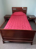 Front view of single wood bed frame with red quilted bed linen and two wooden side tables.