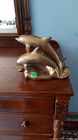 Front view of brass dolphins figurine on wooden furniture, showing three dolphins in a leaping pose.