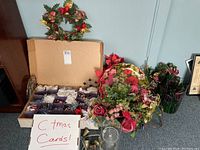 Wide view showing a wreath, floral arrangements, a box of mixed Christmas ornaments, and labels indicating Christmas cards.