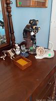 Full image showing bear with cub figurine, dog figurine, lion figurine, horse figurine, ceramic vase with white flowers, and small wooden box