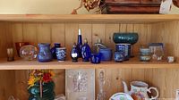 Wooden shelf with a variety of blue and clear glass items including bowls, bottles, and vases with intricate patterns mostly in blue, displayed on top two shelves.