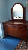 Front view of the dark wood dresser showing three drawers, carved details on legs, and attached arched mirror.