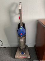 Front full view of Hoover WindTunnel upright vacuum cleaner in metallic gray and blue with dustbin and handle.