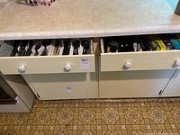 Two kitchen drawers under countertop, one drawer containing cutlery, the other containing wraps and utensils.