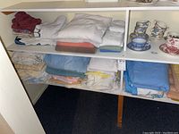 Three shelves with various folded linens including towels, sheets, and blankets in multiple colors.