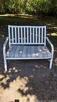 Front facing view of white metal outdoor bench with striped blue and beige cushion, showing slatted backrest and cushion thickness.
