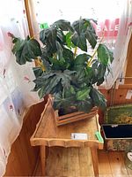 Photo showing the faux leafy green plant in a square pot, sitting on a wooden stand with carved duck motifs on legs.