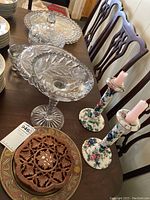 Photo showing glass serving plates including pedestal bowl, covered dish, and decorative plates along with floral painted candle holders on a dining table.