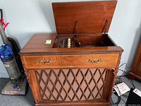 Vintage Electrohome Chipendale III stereo cabinet with open lid showing record player and radio controls inside, with wooden cabinet and vacuum cleaner beside it.