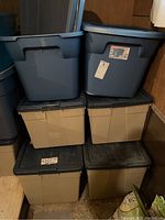 Six Sterilite storage bins stacked - two large blue ones on top, four beige below with black lids.